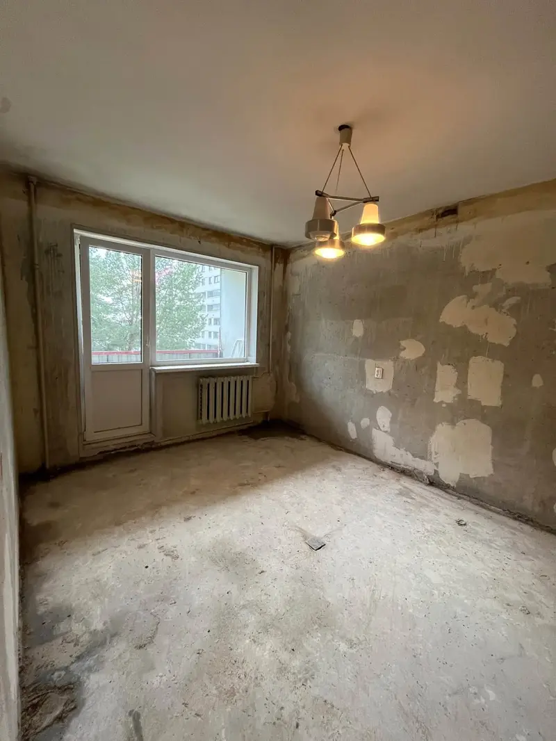 Room with a balcony door after the wallpaper and floor covering were removed, with the window and radiator left in place
