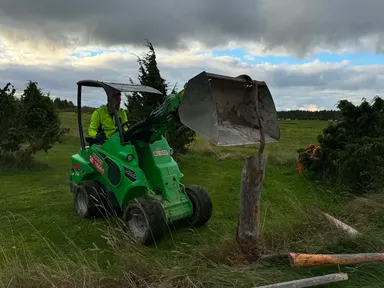 Kompaktlaadur eemaldab vana puitposti maast, kõrval on maas aialatid
