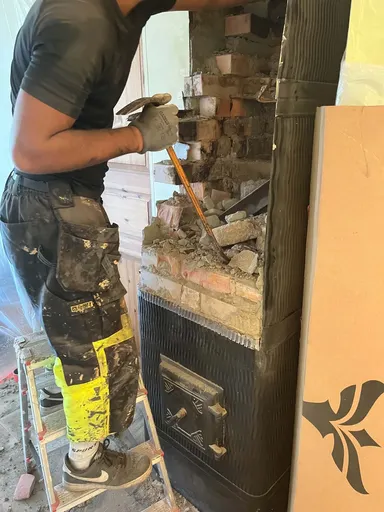 Brickwork of a sheet-metal-clad stove being demolished from a ladder