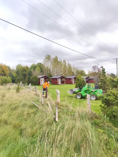 Töötaja võtab puitaeda lahti, maas on eemaldatud latid, taga roheline kompaktlaadur
