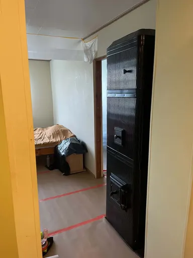 Stove with a black corrugated sheet-metal casing next to a doorway, with the floor covered in paper